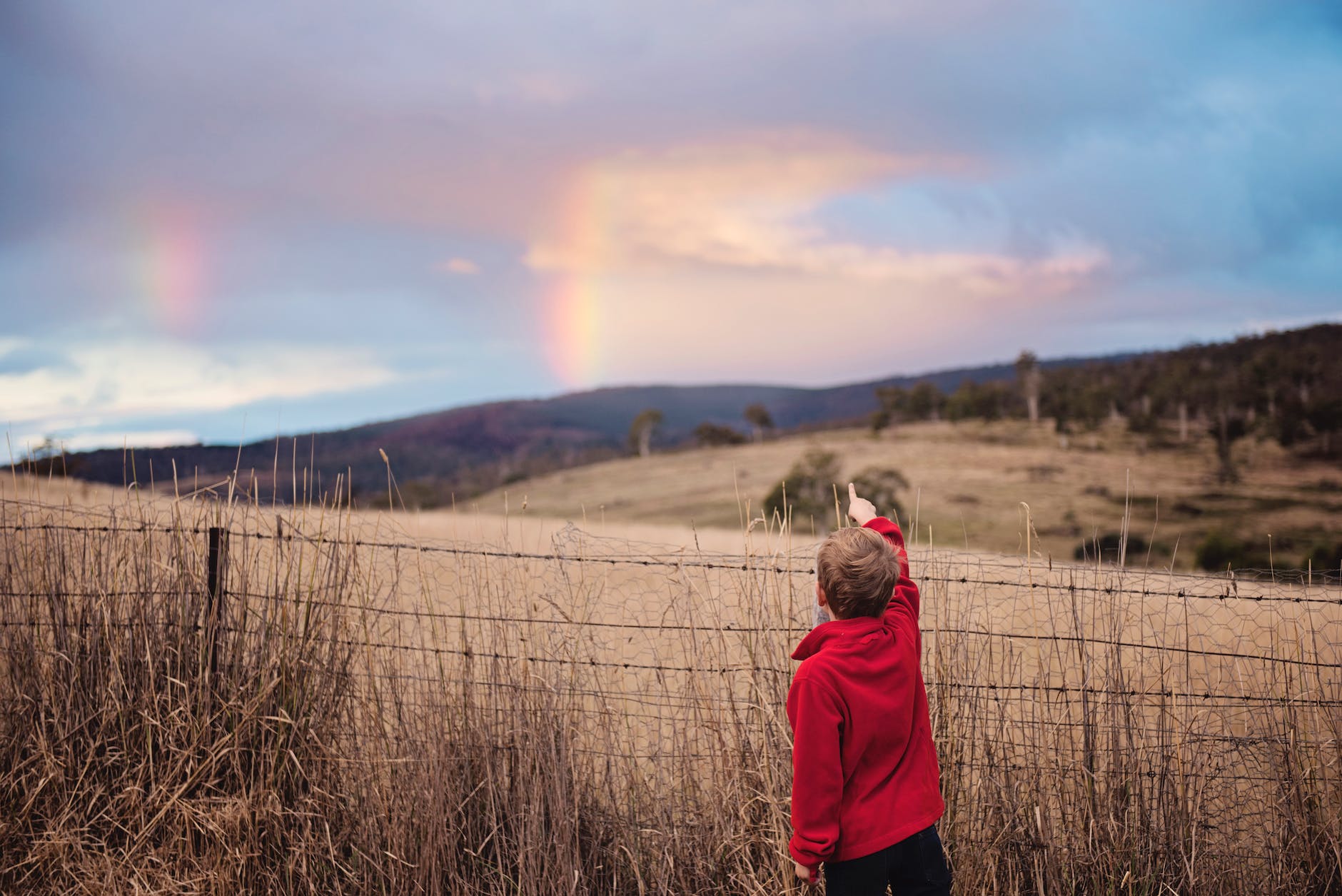 boy standing near fence pointing on the sky